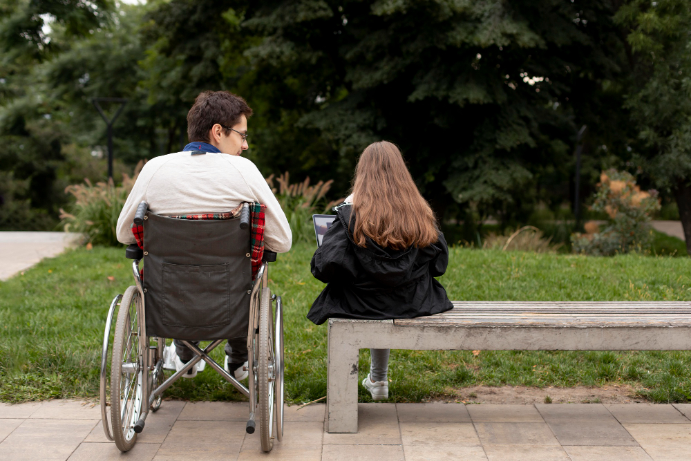 man in a wheelchair next to a girl on a park bench