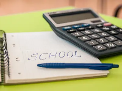an image of a desk with a calculator, blue pen, and a notebook with the word school written on it
