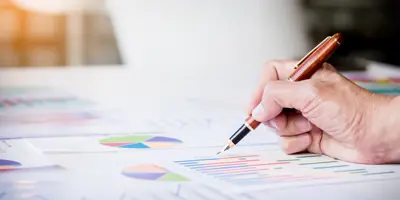 image of a person with a pen pointing at charts on a desk